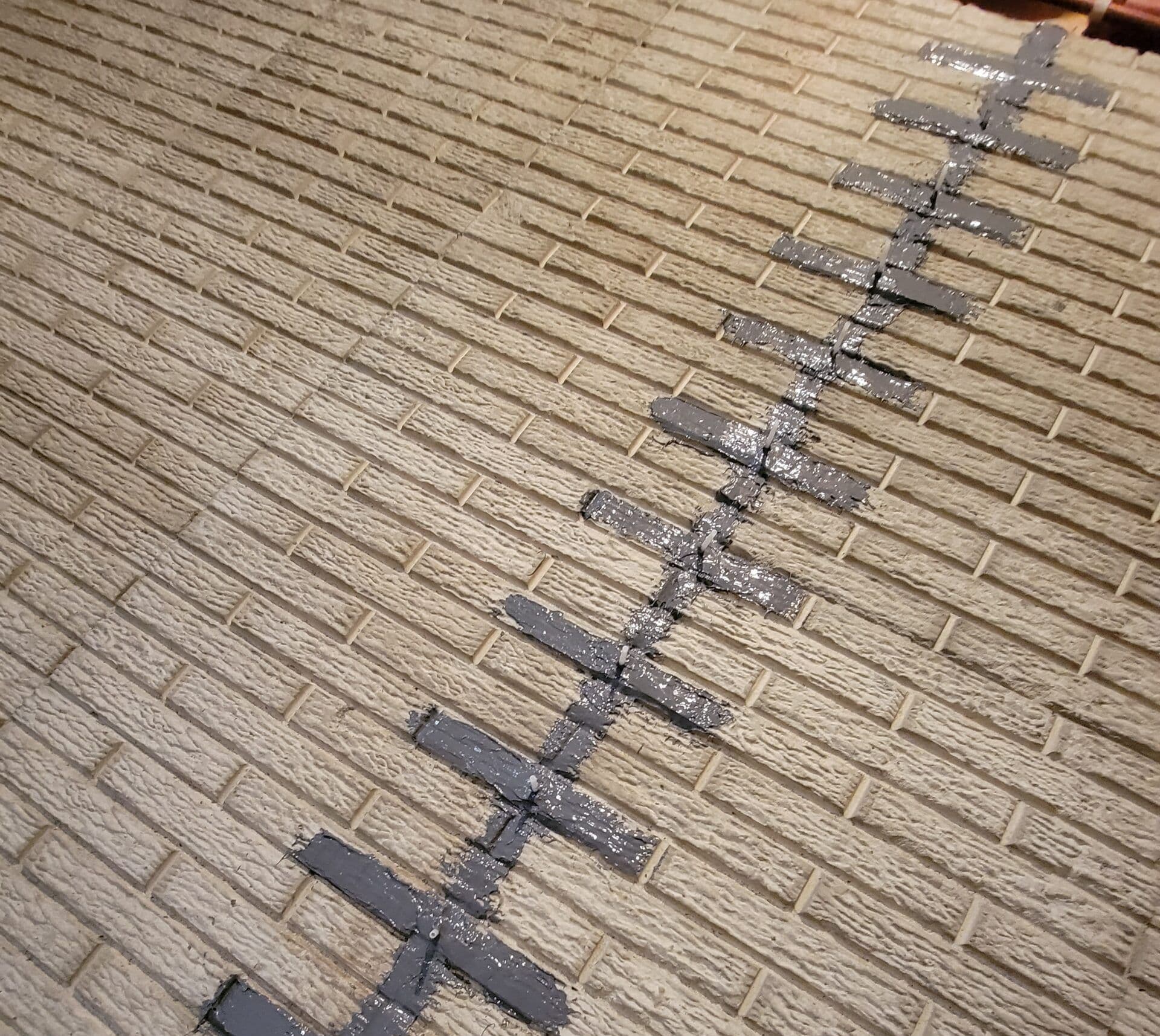 A crack in light tan brick wall that has been injected with a sealant.