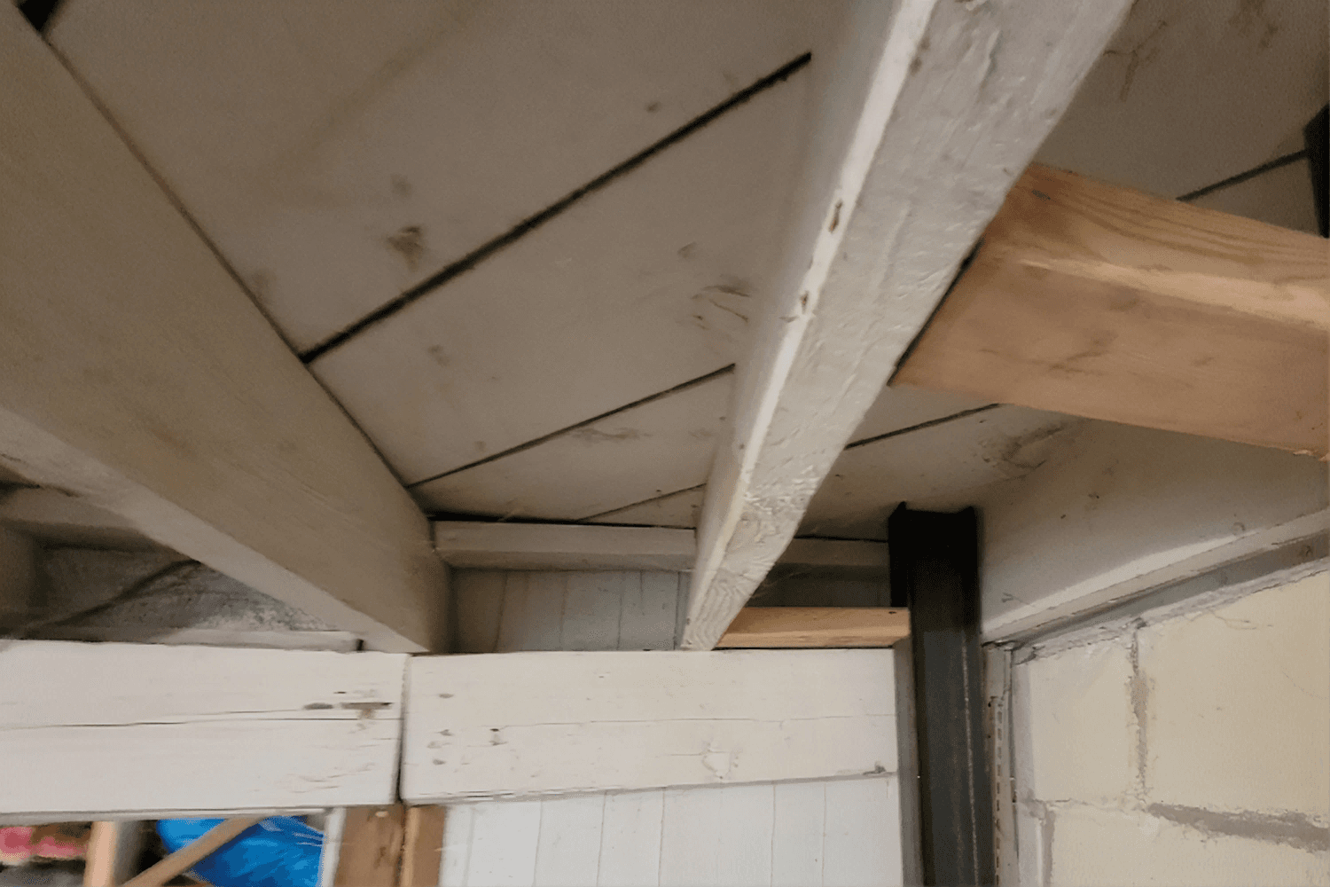 Unfinished ceiling with a crooked wooden joist beam, and white support posts in a basement.