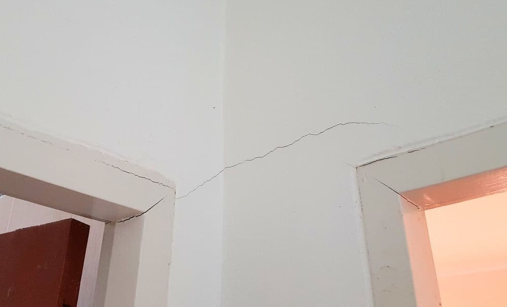 Cracked drywall and ceiling showing structural settlement or damage near doorway frames.