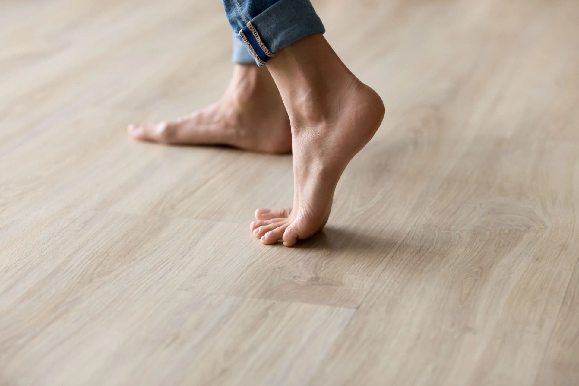 A person in bare feet on light wood laminate flooring wearing rolled denim jeans.