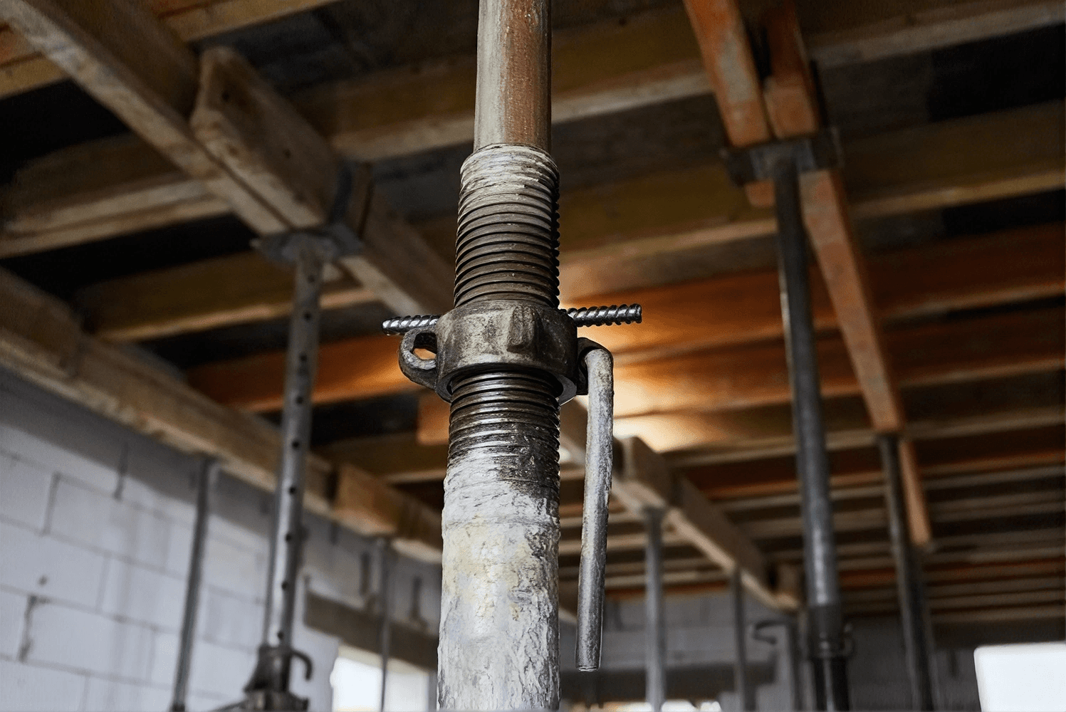 Threaded metal rod with coupling nut and cotter pin installed in a basement with exposed wooden beams.