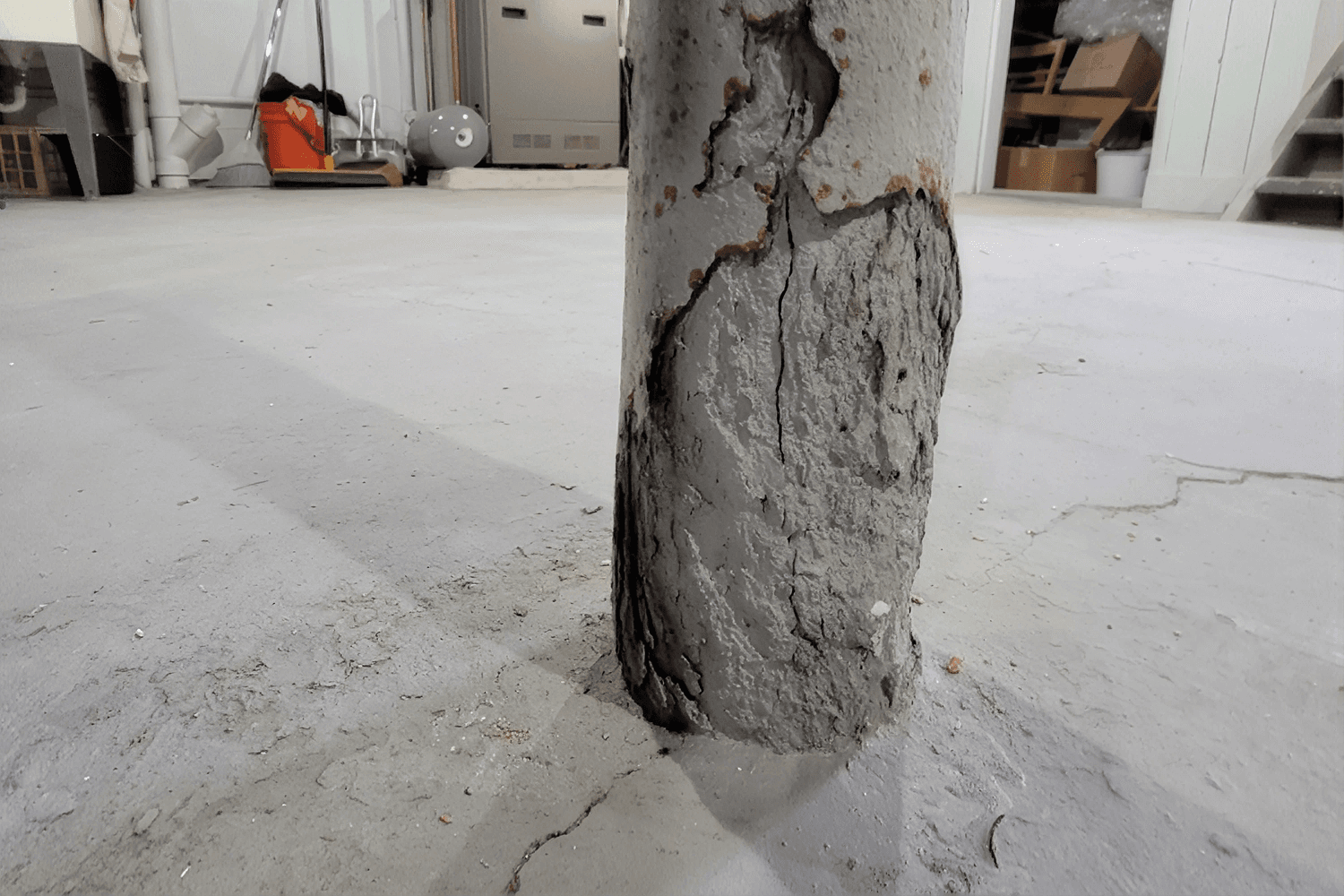 Concrete support column with visible cracks, rust, and deterioration in an unfinished basement.