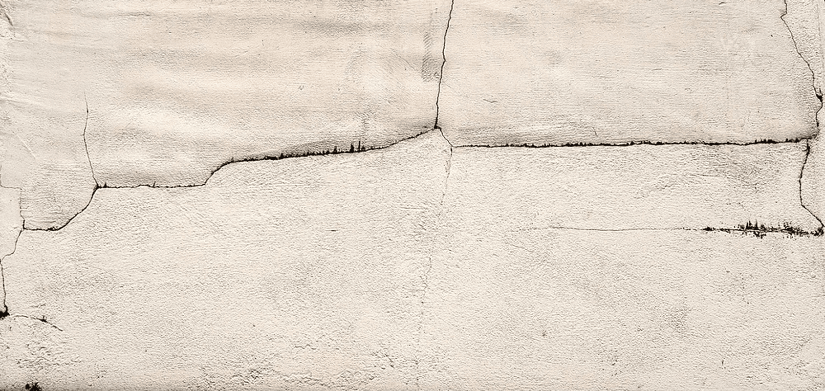 Cracked concrete surface with multiple jagged fissures running horizontally and vertically across the pale grey panel seams.